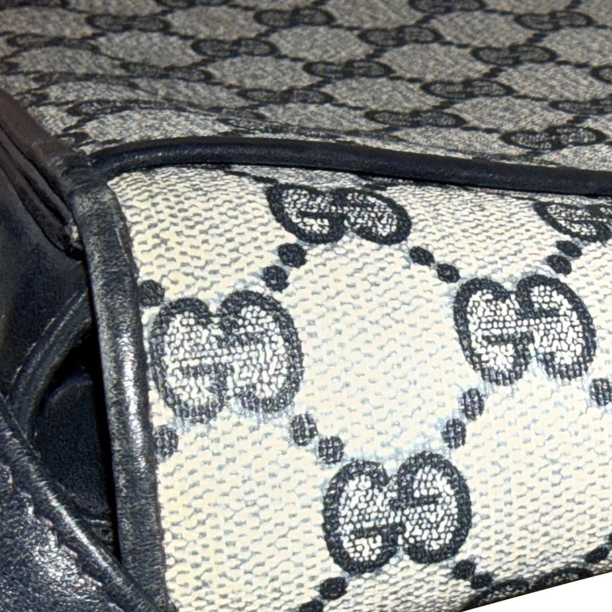 Close-up of the Gucci bag’s monogram panel and navy-trimmed corner, showing surface and edge wear.