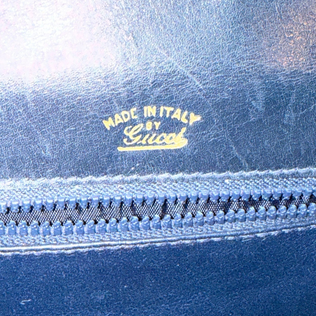 Gold Made in Italy by Gucci stamp above the interior zipper, with scratches visible on the blue lining.